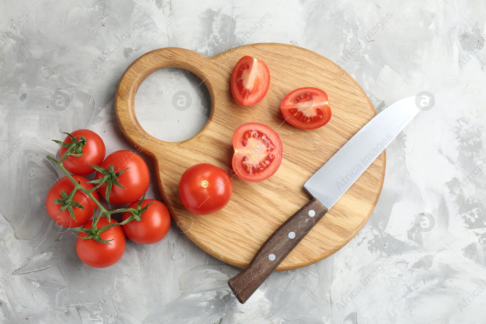 Photo of Cutting board with tomatoes and knife on grey textured table, top view