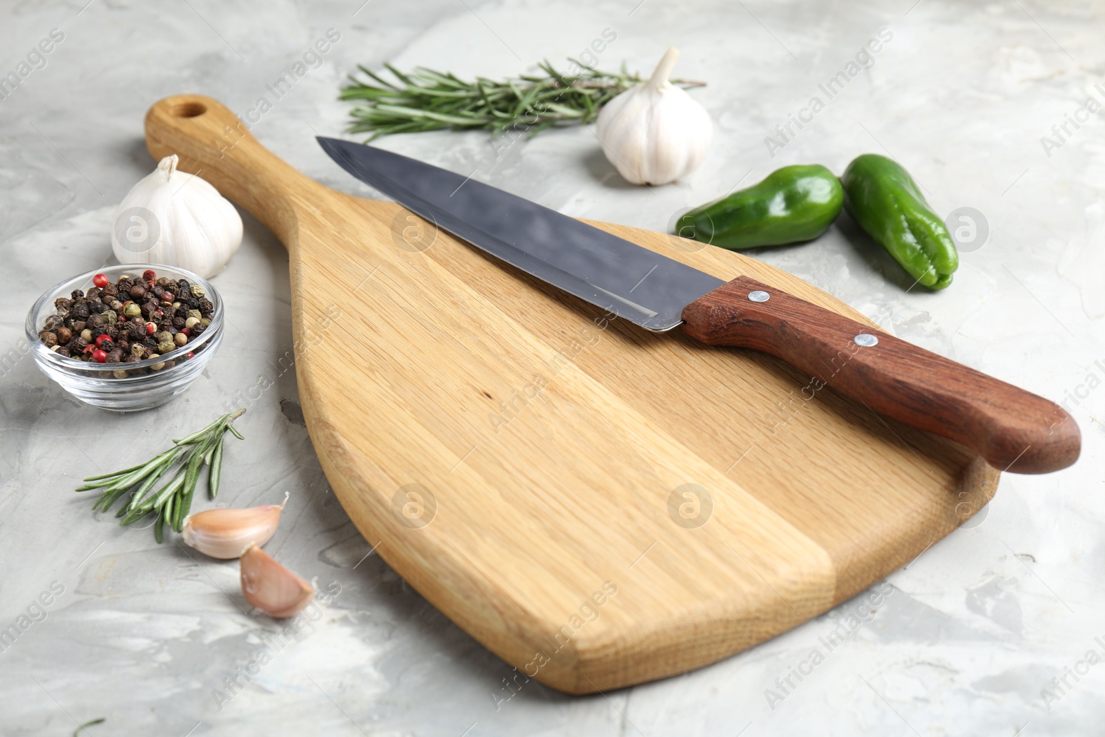 Photo of Cutting board with knife and spices on grey textured table, closeup