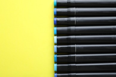 Photo of Color double sided markers on yellow background, top view. Space for text