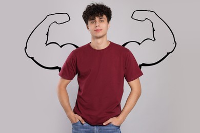 Image of Handsome young man with drawing of strong arms behind him on grey background