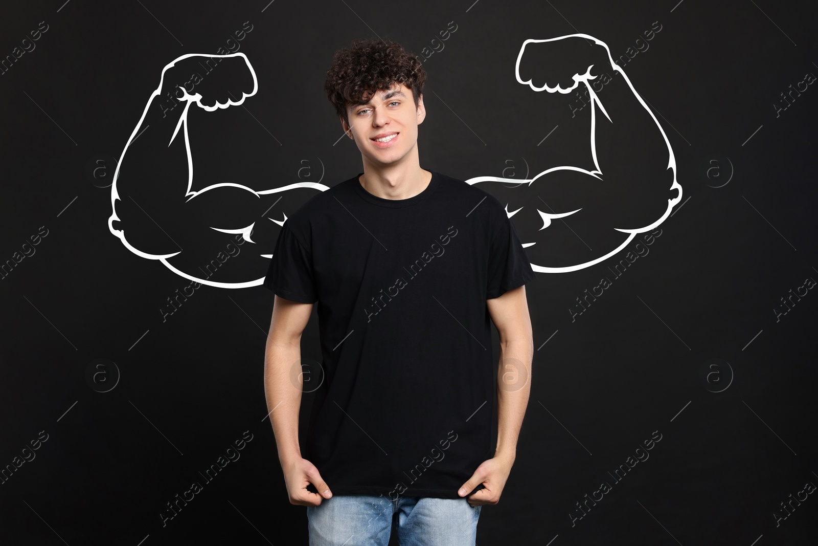 Image of Handsome young man with drawing of strong arms behind him on black background