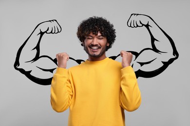 Image of Happy young man with drawing of strong arms behind him on grey background