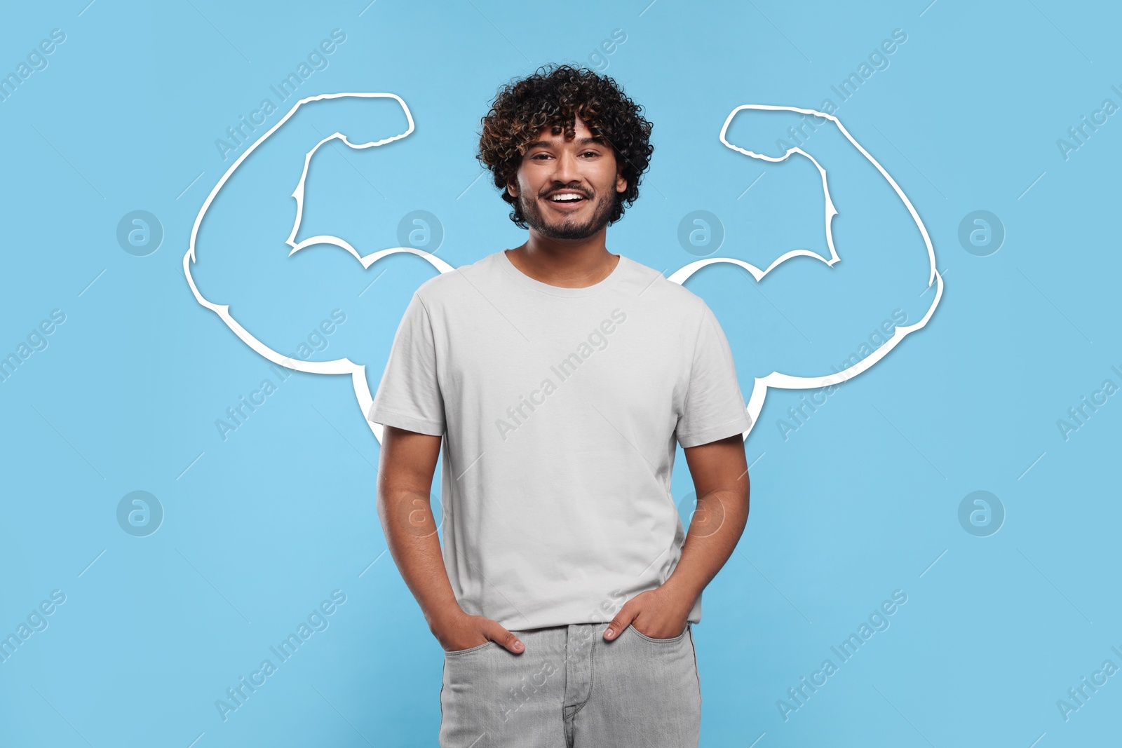 Image of Happy young man with drawing of strong arms behind him on light blue background