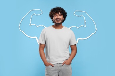 Image of Happy young man with drawing of strong arms behind him on light blue background