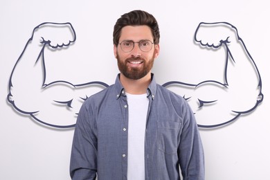 Image of Handsome man with drawing of strong arms behind him on white background