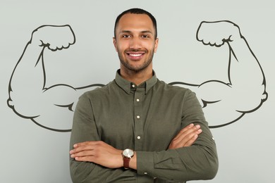 Image of Handsome young man with drawing of strong arms behind him on grey background