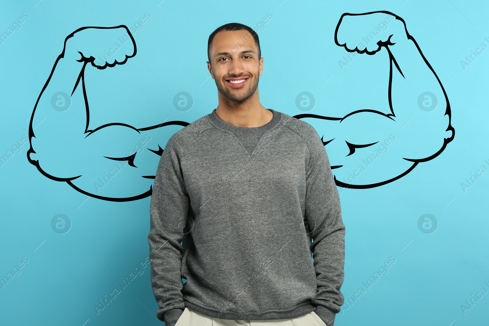 Image of Handsome young man with drawing of strong arms behind him on light blue background