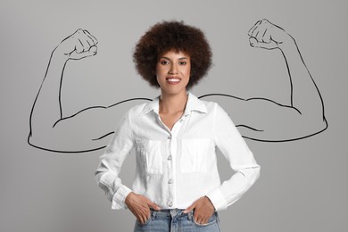 Image of Confident beautiful woman with drawing of strong arms behind her on grey background