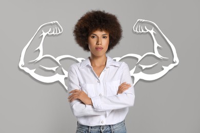 Confident beautiful woman with drawing of strong arms behind her on grey background