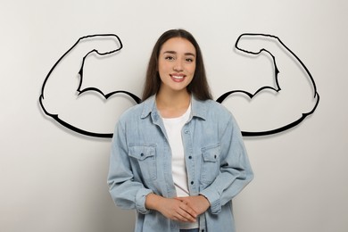 Image of Beautiful young woman with drawing of strong arms behind her on grey background