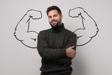 Handsome young man with drawing of strong arms behind him on grey background