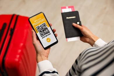 Image of Tourist with passport, flight ticket and mobile phone indoors, above view. Immunity passport app with QR code on device screen