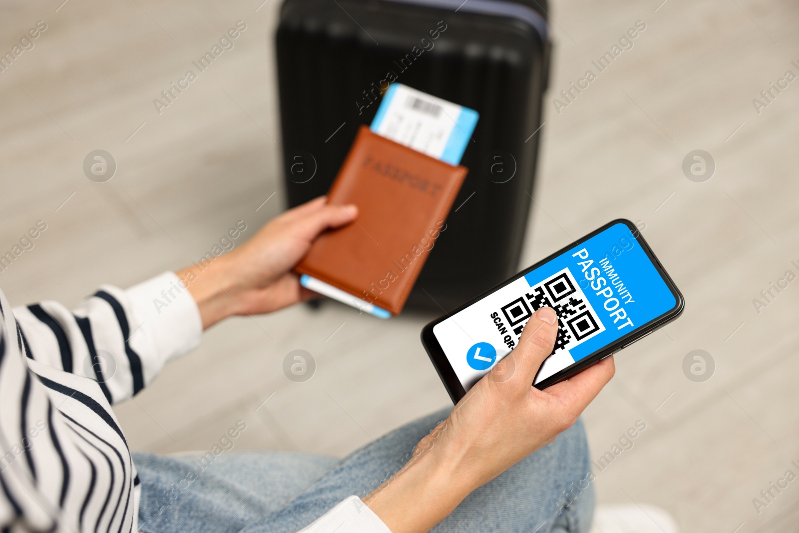 Image of Tourist with passport, flight ticket and mobile phone indoors, above view. Immunity passport app with QR code on device screen