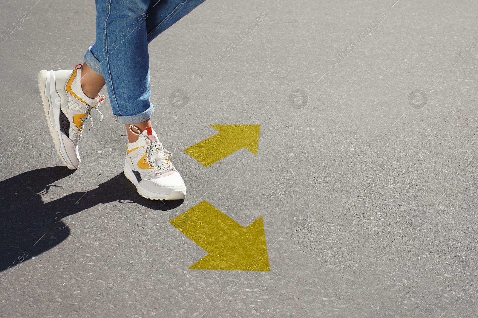 Image of Woman walking on asphalt road with yellow arrows pointing in different directions, closeup. Concepts of choice, decision, alternative way