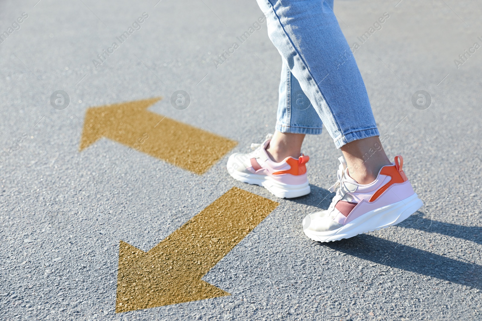 Image of Woman walking on asphalt road with orange arrows pointing in different directions, closeup. Concepts of choice, decision, alternative way