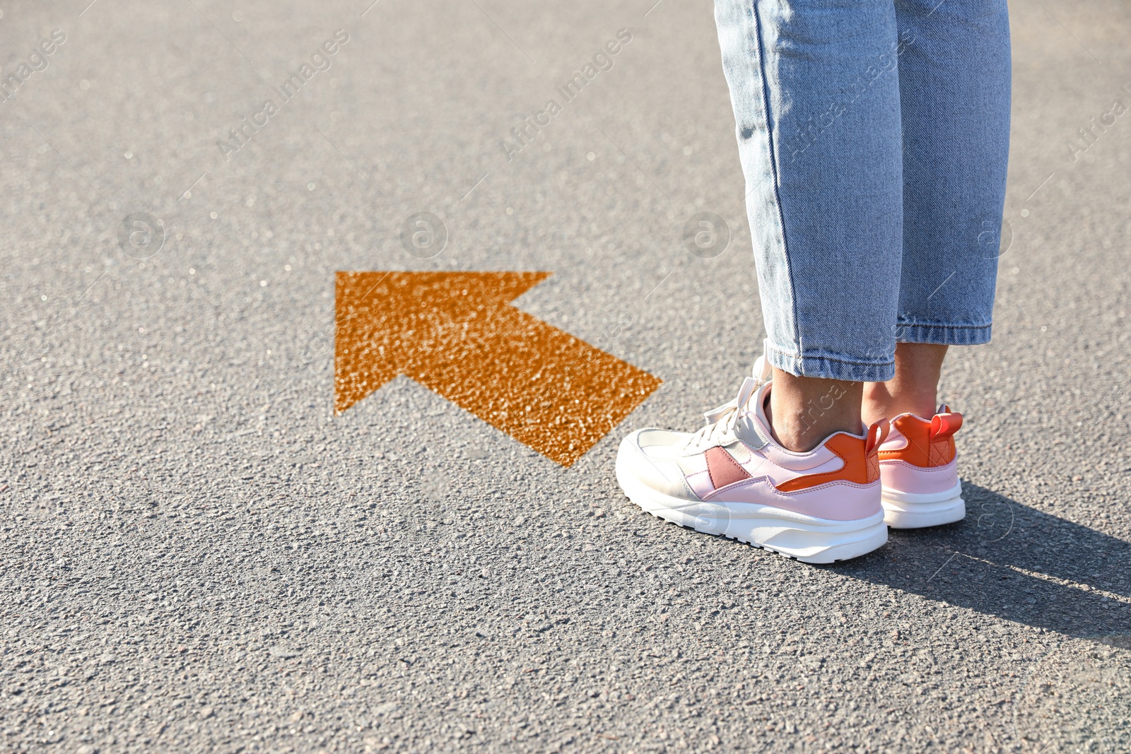 Image of Woman standing near orange arrow on asphalt road, closeup. Concepts of choice, decision, moving forward