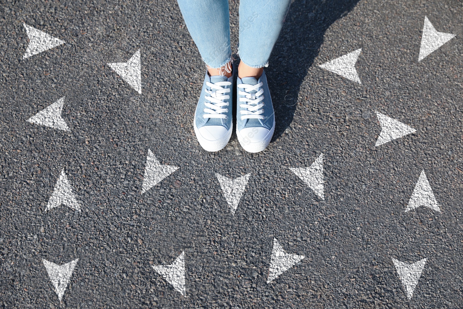 Image of Woman standing near white arrows on asphalt road, closeup. Concepts of choice, decision, different way, alternative