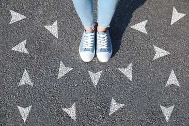 Image of Woman standing near white arrows on asphalt road, closeup. Concepts of choice, decision, different way, alternative