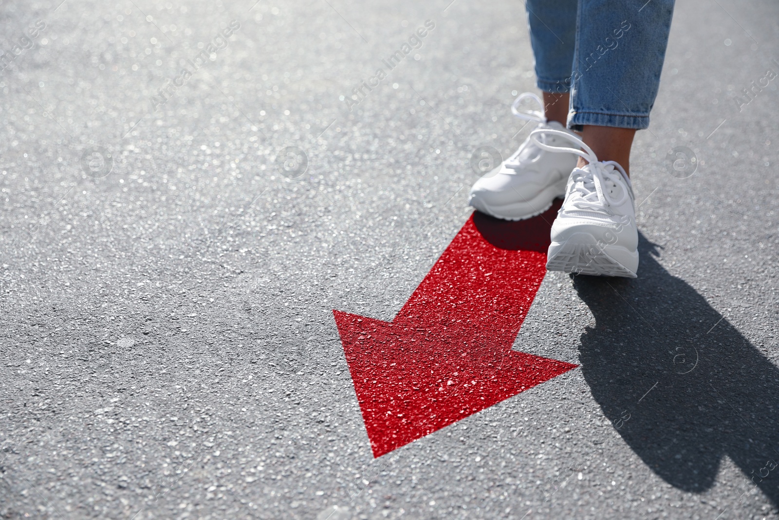 Image of Woman walking on asphalt road with red arrow, closeup. Concepts of choice, decision, moving forward