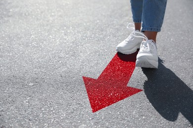 Image of Woman walking on asphalt road with red arrow, closeup. Concepts of choice, decision, moving forward