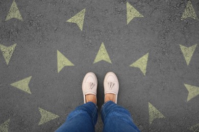 Image of Woman standing near yellow arrows on asphalt road, closeup. Concepts of choice, decision, different way, alternative