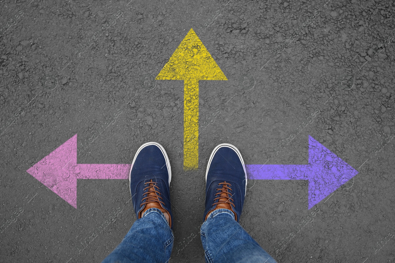 Image of Man standing near colorful arrows on asphalt road, closeup. Concepts of choice, decision, different way, alternative