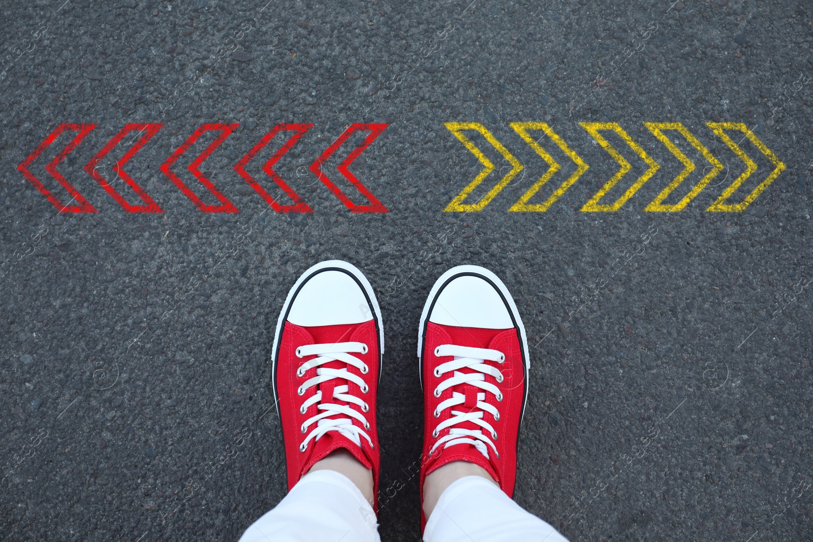 Image of Woman standing near red and yellow arrows pointing in different directions on asphalt road, closeup. Concepts of choice, decision, alternative way