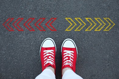 Image of Woman standing near red and yellow arrows pointing in different directions on asphalt road, closeup. Concepts of choice, decision, alternative way