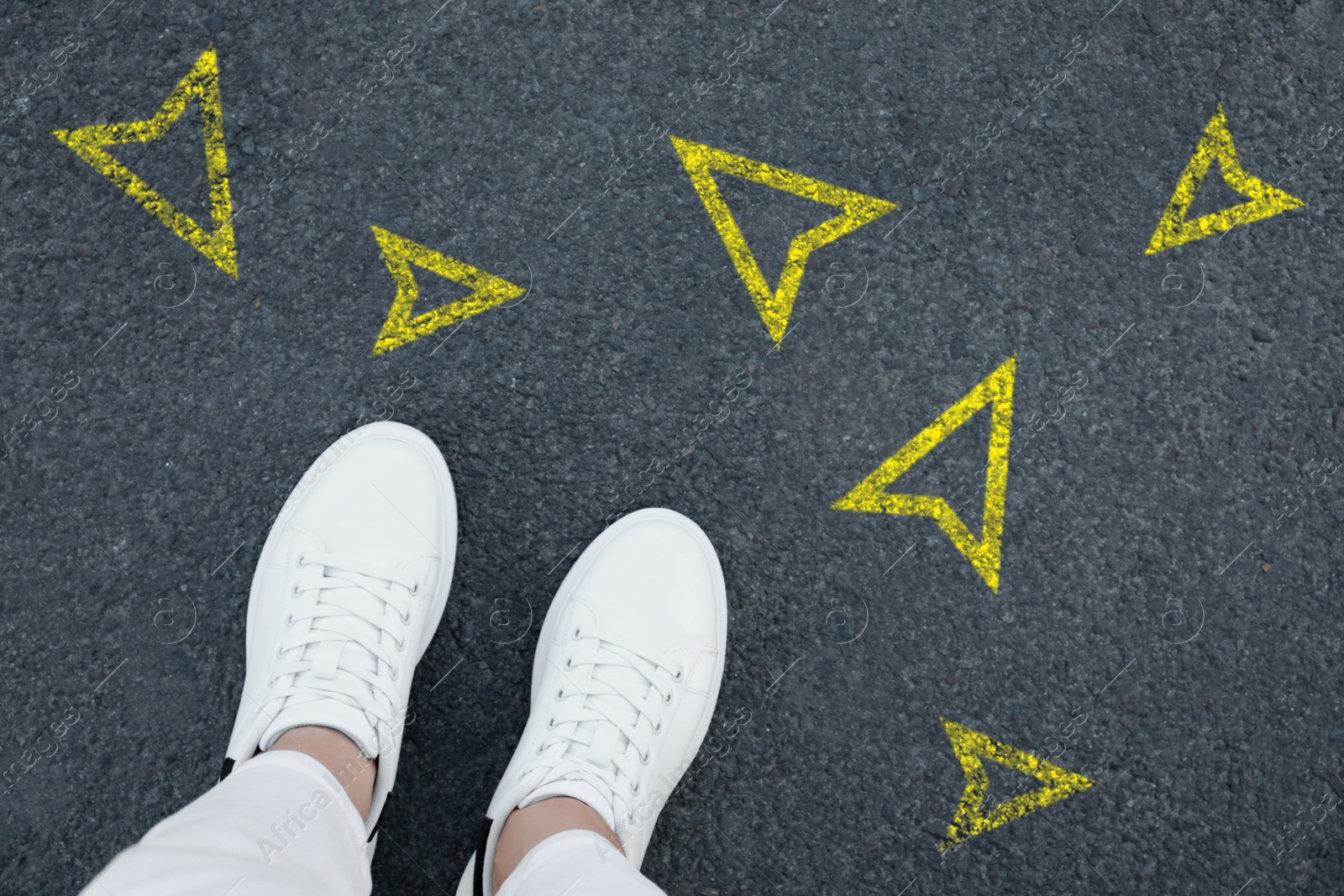 Image of Woman standing near yellow arrows pointing in different directions on asphalt road, closeup. Concepts of choice, decision, alternative way