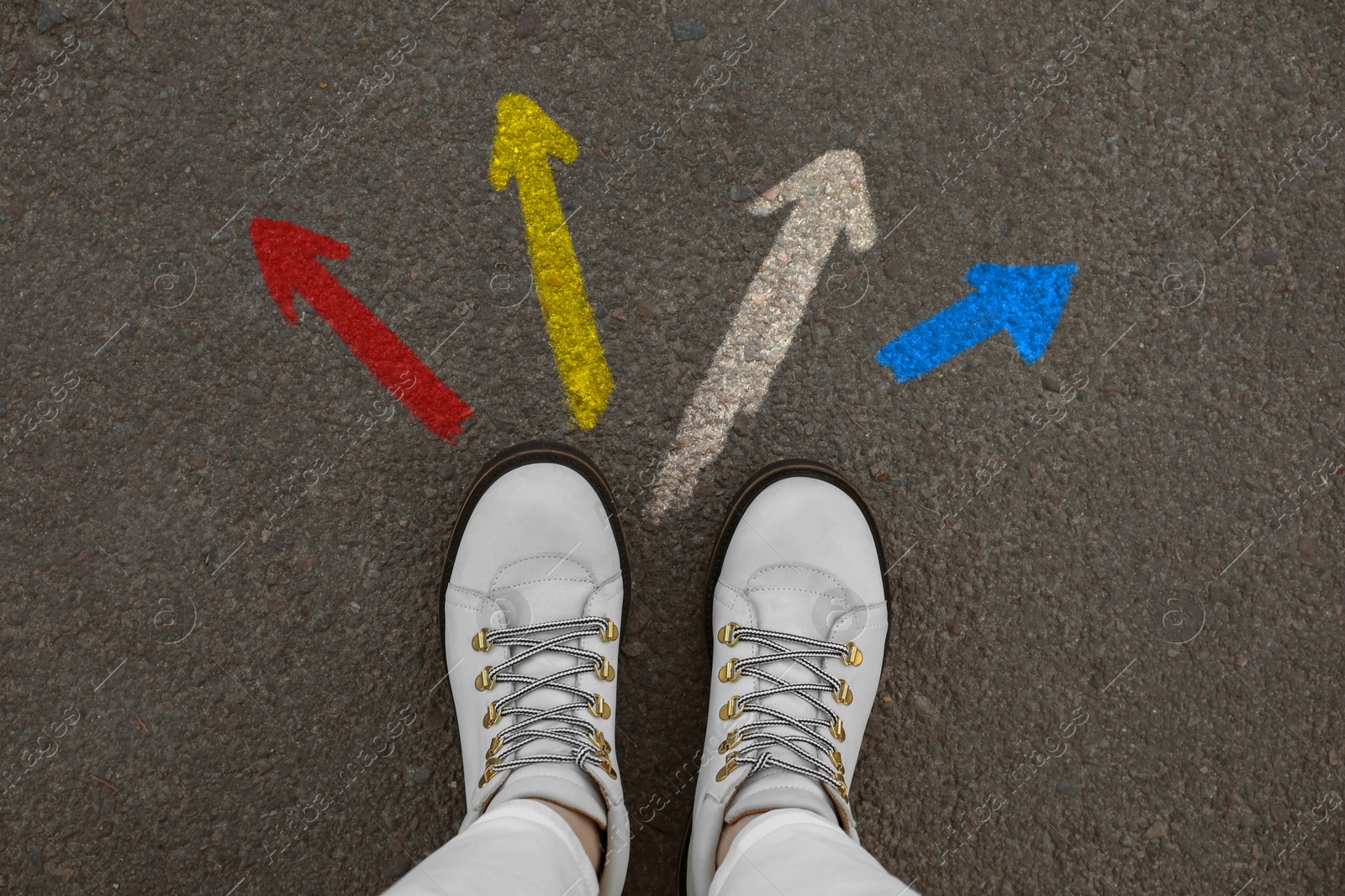 Image of Woman standing near colorful arrows pointing in different directions on asphalt road, closeup. Concepts of choice, decision, alternative way