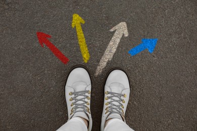 Image of Woman standing near colorful arrows pointing in different directions on asphalt road, closeup. Concepts of choice, decision, alternative way