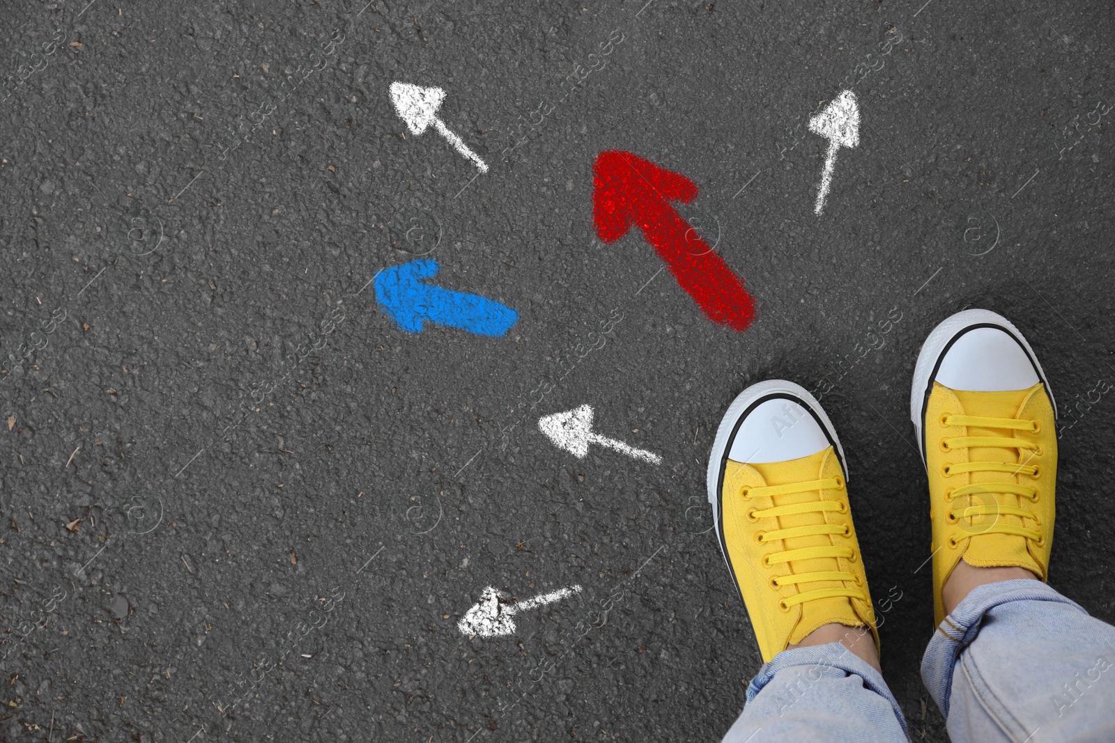 Image of Woman standing near colorful arrows pointing in different directions on asphalt road, closeup. Concepts of choice, decision, alternative way