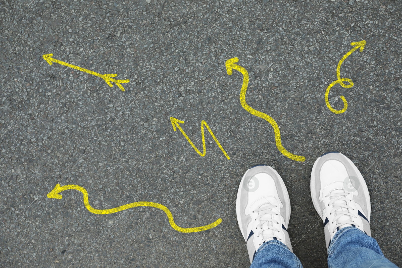 Image of Man standing near yellow arrows pointing in different directions on asphalt road, closeup. Concepts of choice, decision, alternative way