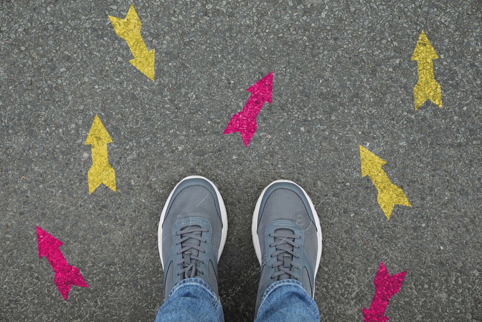 Image of Man standing near yellow and pink arrows pointing in different directions on asphalt road, closeup. Concepts of choice, decision, alternative way