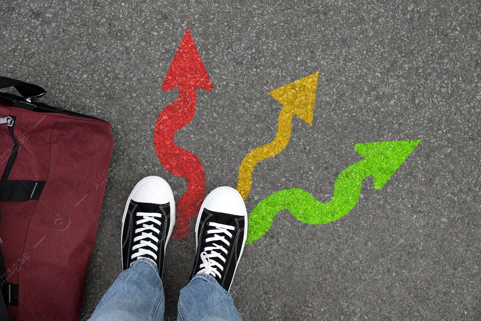 Image of Man standing near colorful arrows pointing in different directions on asphalt road, closeup. Concepts of choice, decision, alternative way