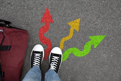 Image of Man standing near colorful arrows pointing in different directions on asphalt road, closeup. Concepts of choice, decision, alternative way