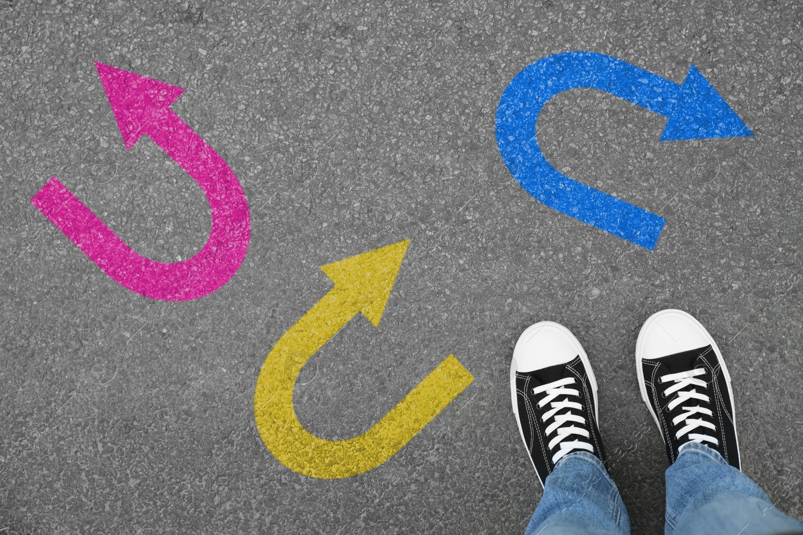 Image of Man standing near colorful arrows pointing in different directions on asphalt road, closeup. Concepts of choice, decision, alternative way