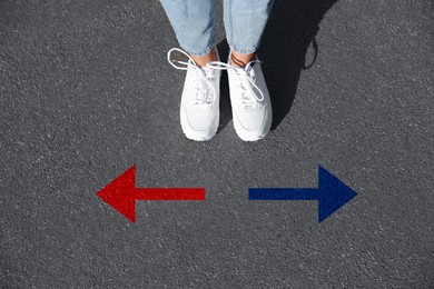 Image of Woman standing near red and blue arrows pointing in different directions on asphalt road, closeup. Concepts of choice, decision, alternative way