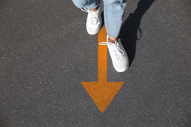 Image of Woman walking on asphalt road with orange arrow, closeup. Concepts of choice, decision, moving forward