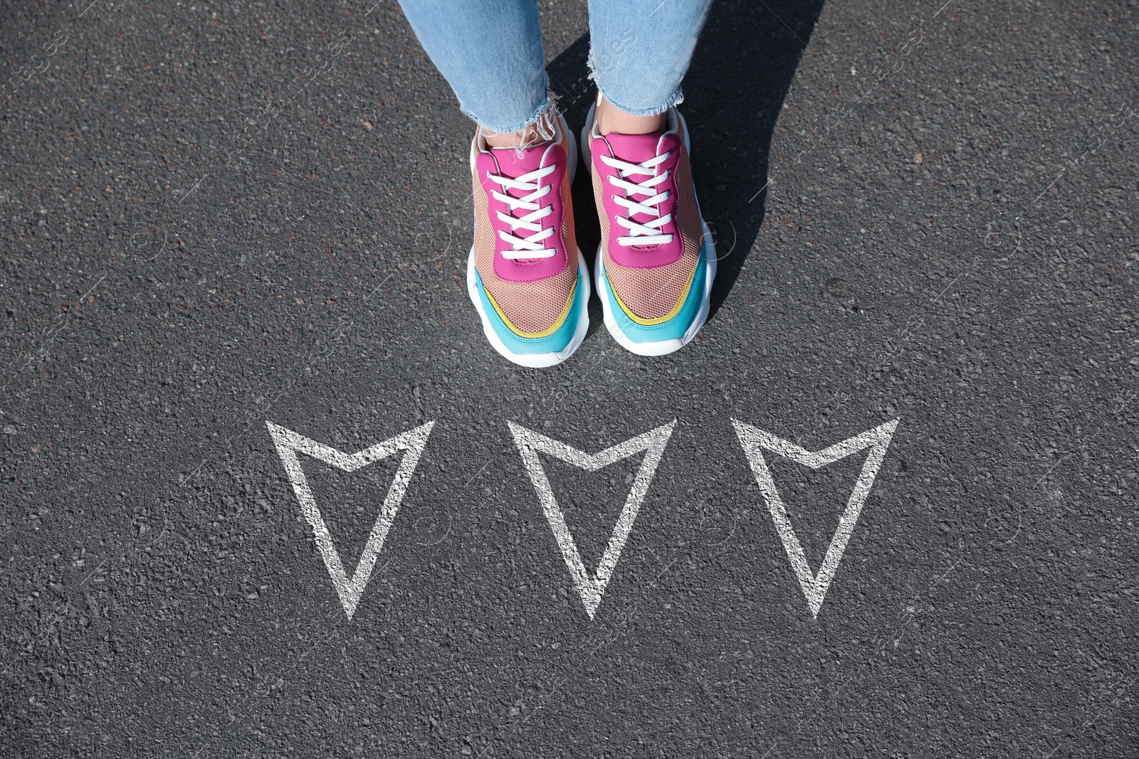 Image of Woman standing near white arrows on asphalt road, closeup. Concepts of choice, decision, moving forward