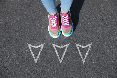 Image of Woman standing near white arrows on asphalt road, closeup. Concepts of choice, decision, moving forward