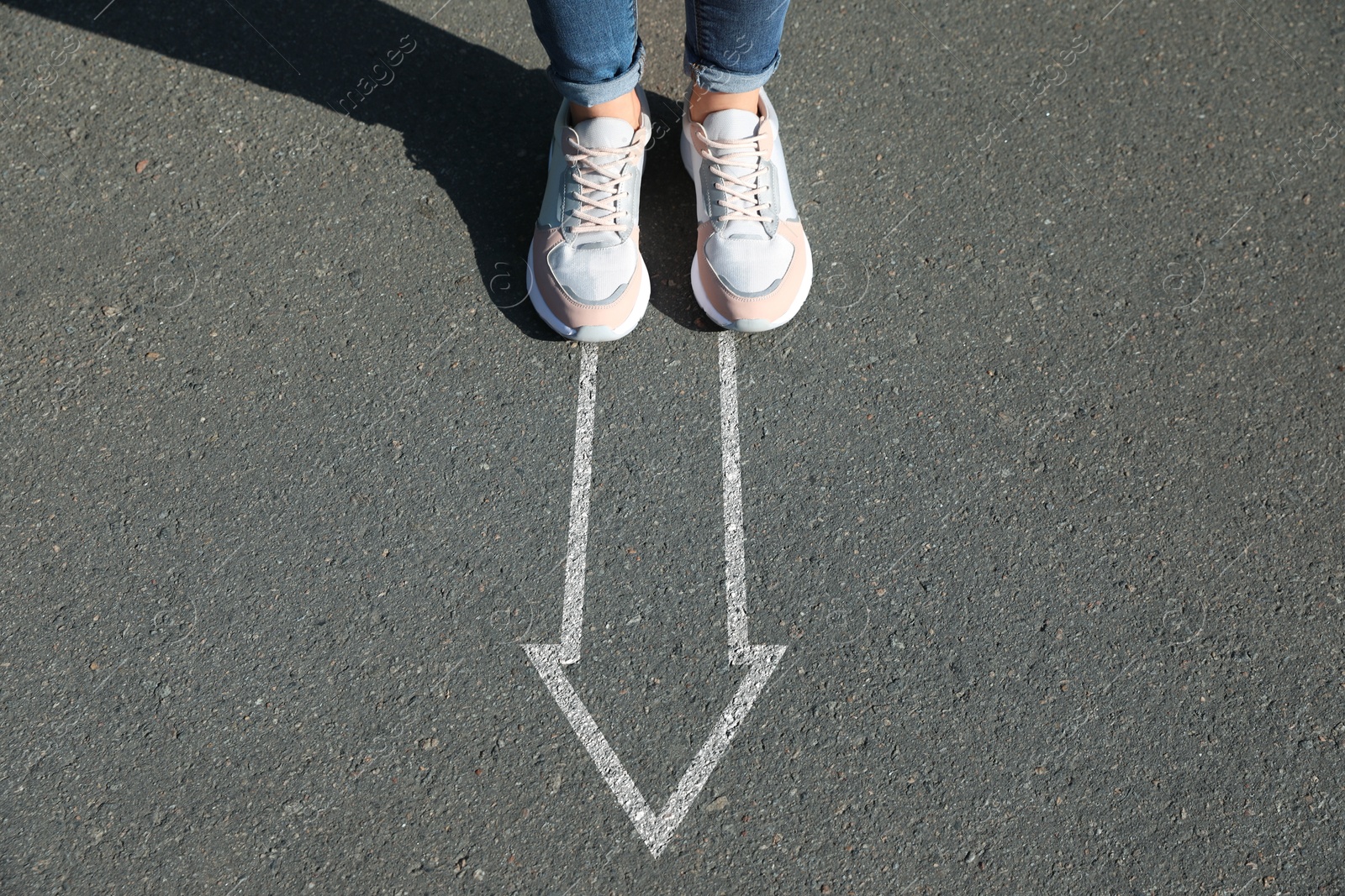 Image of Woman standing near white arrow on asphalt road, closeup. Concepts of choice, decision, moving forward