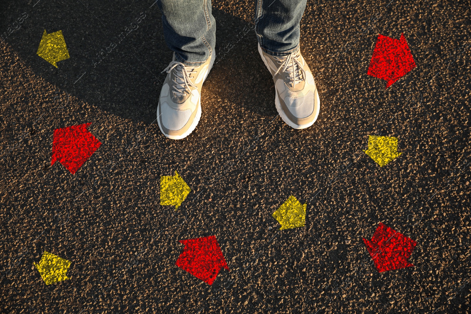 Image of Man standing near red and yellow arrows pointing in different directions on asphalt road, closeup. Concepts of choice, decision, alternative way