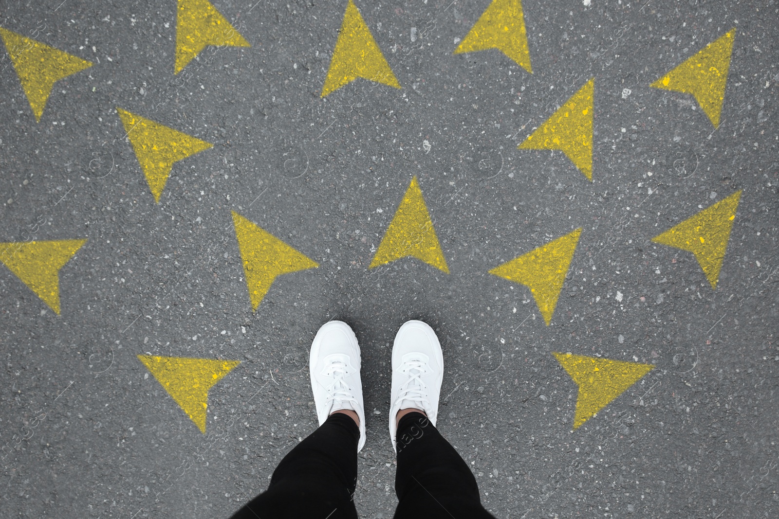 Image of Woman standing near yellow arrows pointing in different directions on asphalt road, closeup. Concepts of choice, decision, alternative way