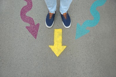 Image of Man standing near colorful arrows pointing in different directions on asphalt road, closeup. Concepts of choice, decision, alternative way