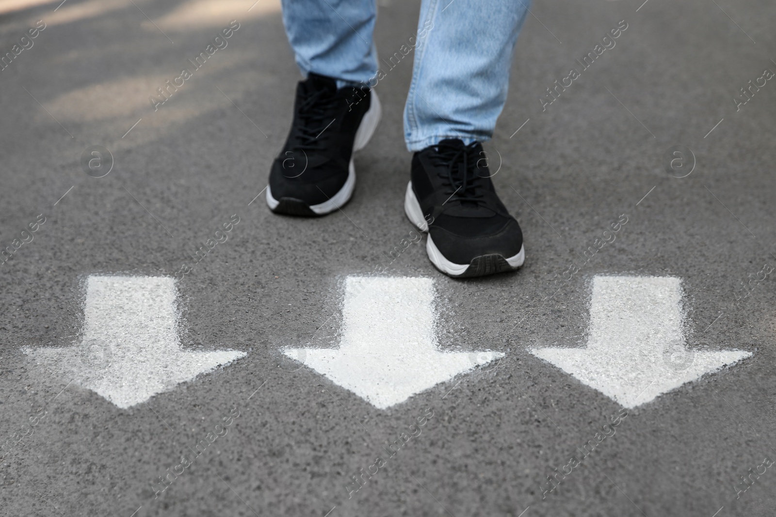 Image of Man walking on asphalt road with white arrows, closeup. Concepts of choice, decision, moving forward