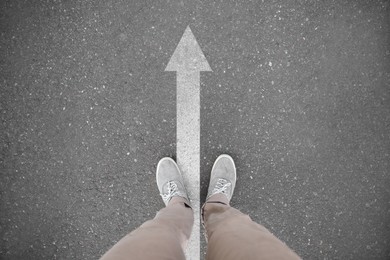 Image of Man standing near white arrow on asphalt road, closeup. Concepts of choice, decision, moving forward