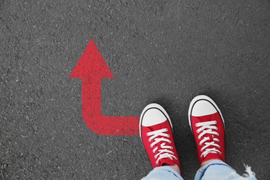 Image of Woman standing near red arrow on asphalt road, closeup. Concepts of choice, decision, moving forward