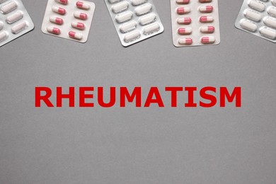 Image of Rheumatism. Different pills in blisters and word on grey background, top view