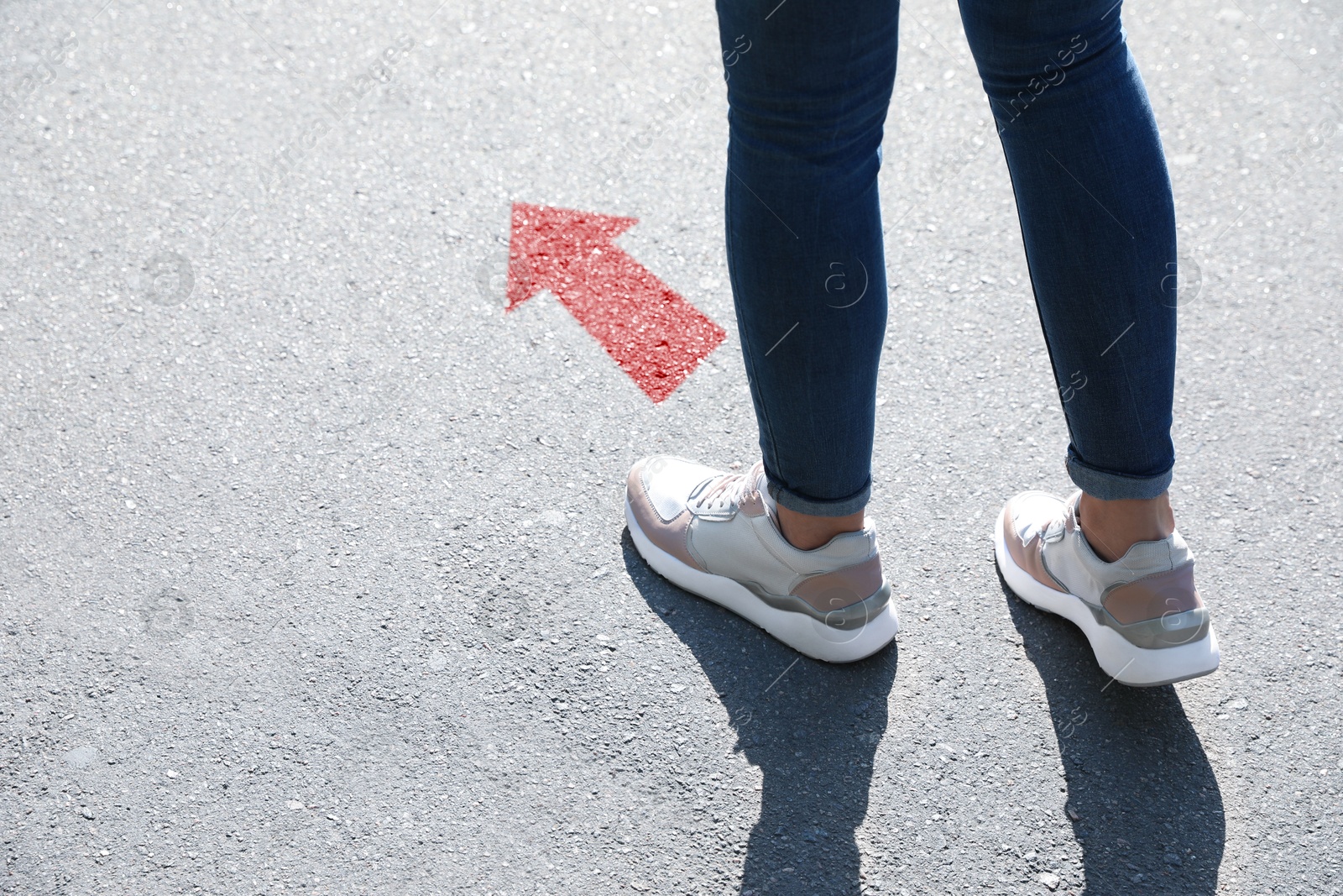 Image of Woman walking on asphalt road with red arrow, closeup. Concepts of choice, decision, moving forward